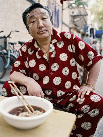 Foto Lámina fotográfica Man in Silk Pajamas Eats a Bowl of Noodles on the Street de Eightfish, 41x30 in. foto 864451